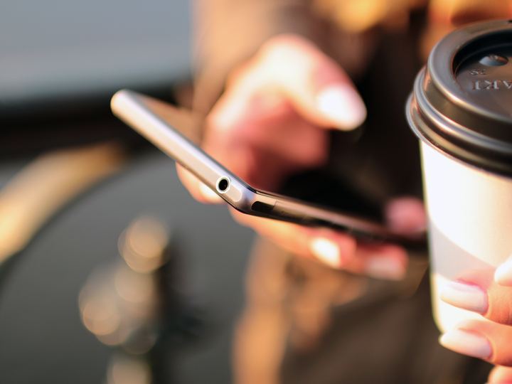 Hands holding a smartphone next to a cup of coffee